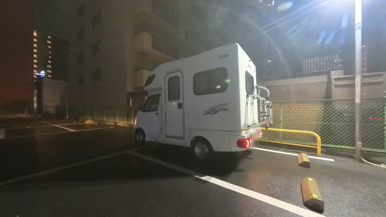 雨に濡れたコインパーキングに停めた白い軽キャンピングカー・ラクーン